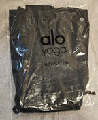 Black yoga mat in a clear plastic bag with 'alo yoga' branding on a textured surface.
