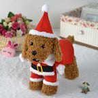 Plush toy dog in a Santa outfit on a light surface with flowers and a box in the background.