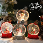 Decorative snow globes with Christmas scenes on a snowy surface with a tree in the background.